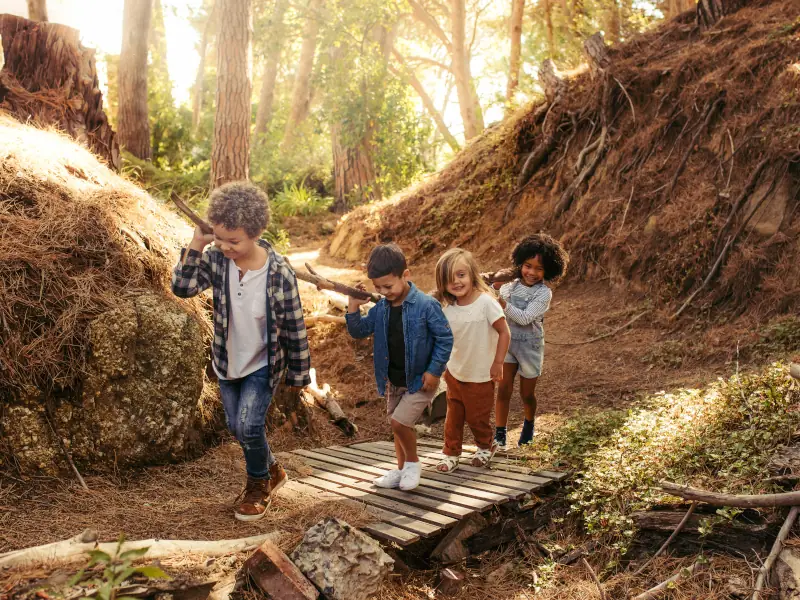 Children carrying a long stick across a bridge in the woods