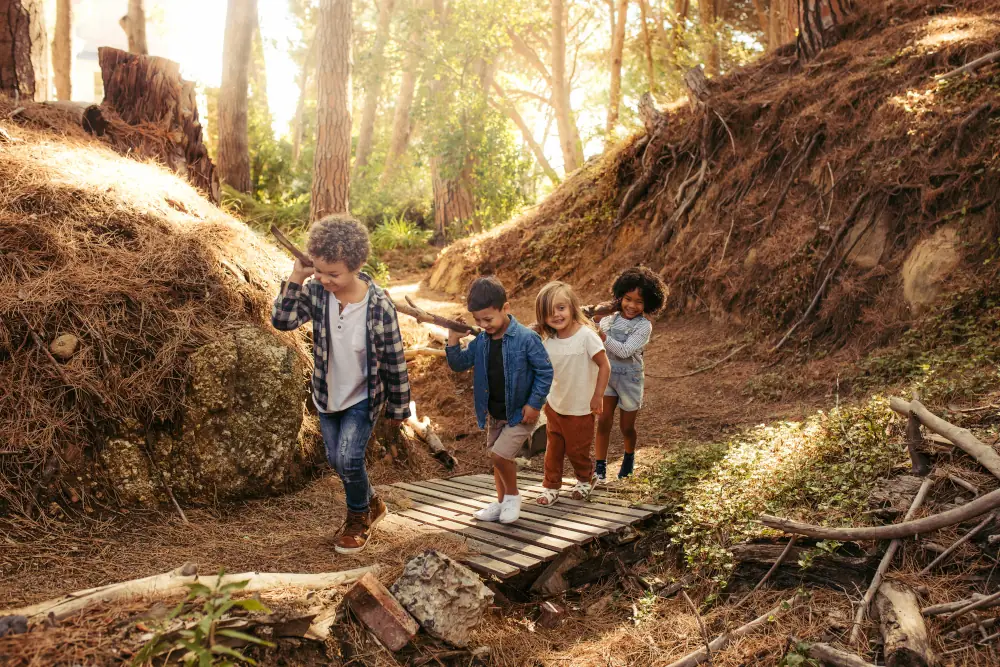 Children carrying a long stick across a bridge in the woods